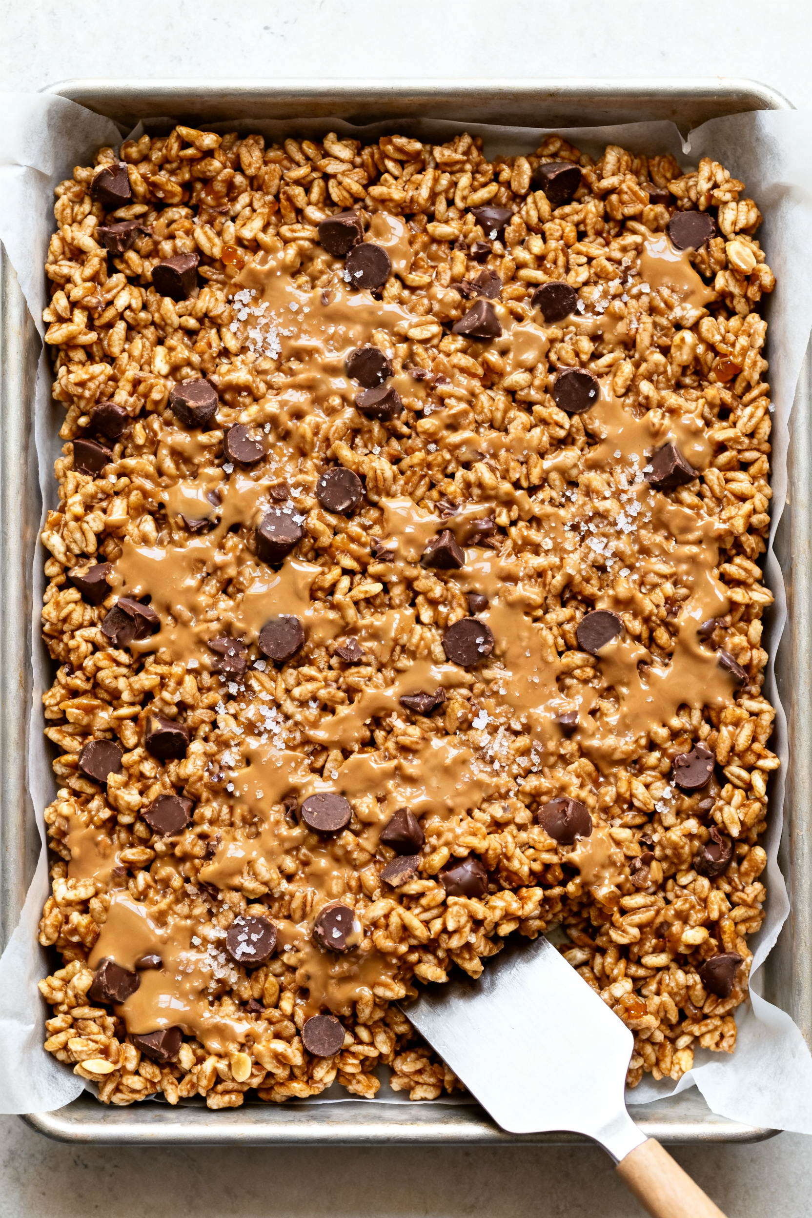 Cooking process: Peanut butter chocolate rice crispy mixture being pressed evenly into a parchment-l