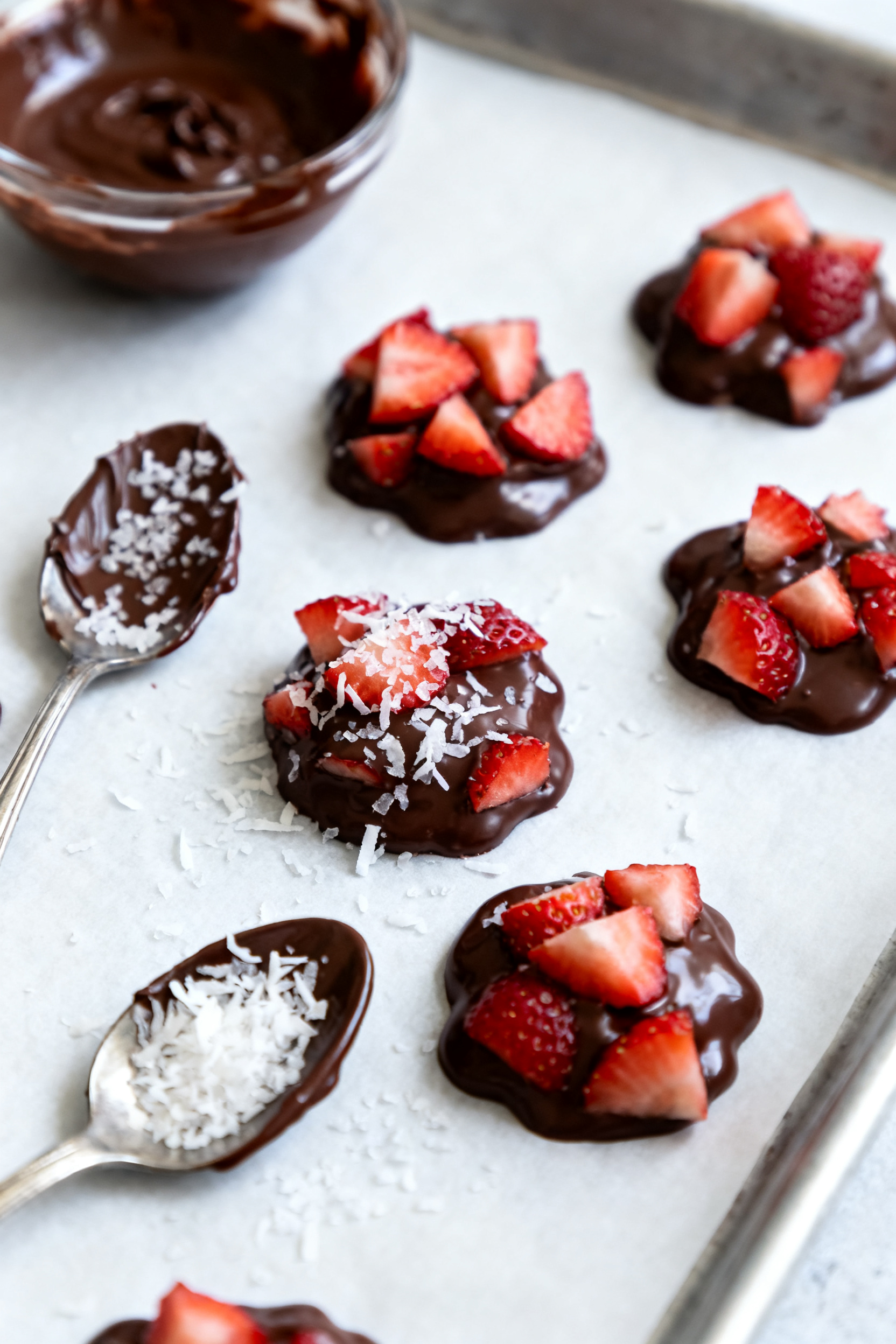 Process-in-action shot: strawberry chocolate clusters setting on a parchment-lined tray, glossy semi